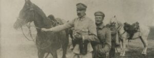 Józef Piłsudski trzyma za uzdę Kasztankę, w drugim ręku lornetkę. Za nim stoi adiutant.