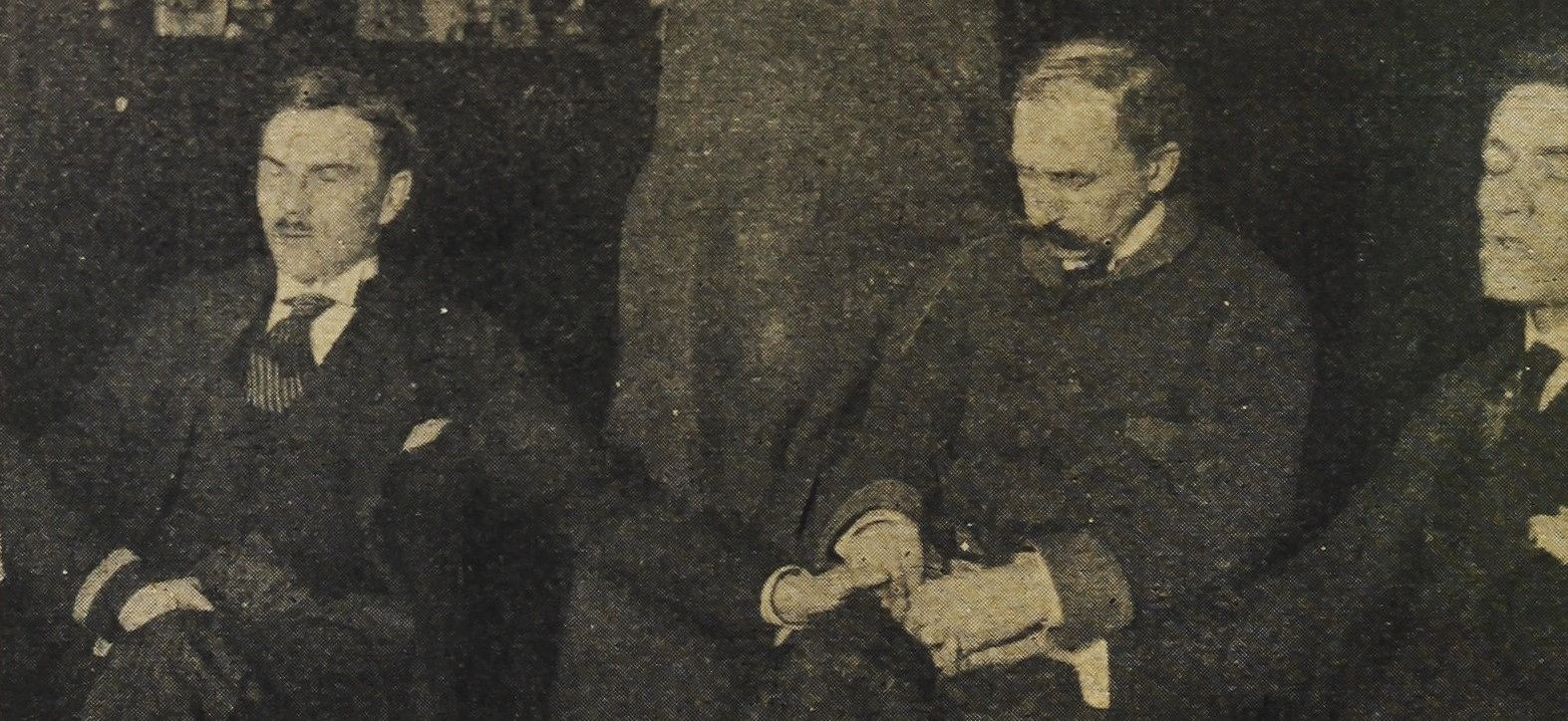 Franek Kluski podczas seansu spirytystycznego. Siedzi, trzyma za dłonie dwóch mężczyzn siedzących obok niego, wszyscy mają zamknięte oczy.