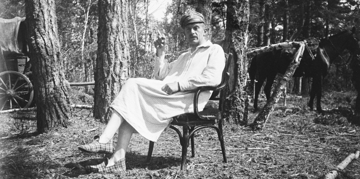 Stanisław Janowski siedzi na krześle w koszuli nocnej i kapciach i pali papierosa, patrzy w kierunku obiektywu. Na głowie ma legionową maciejówkę. Cała scena ma miejsce w lesie w porze letniej.